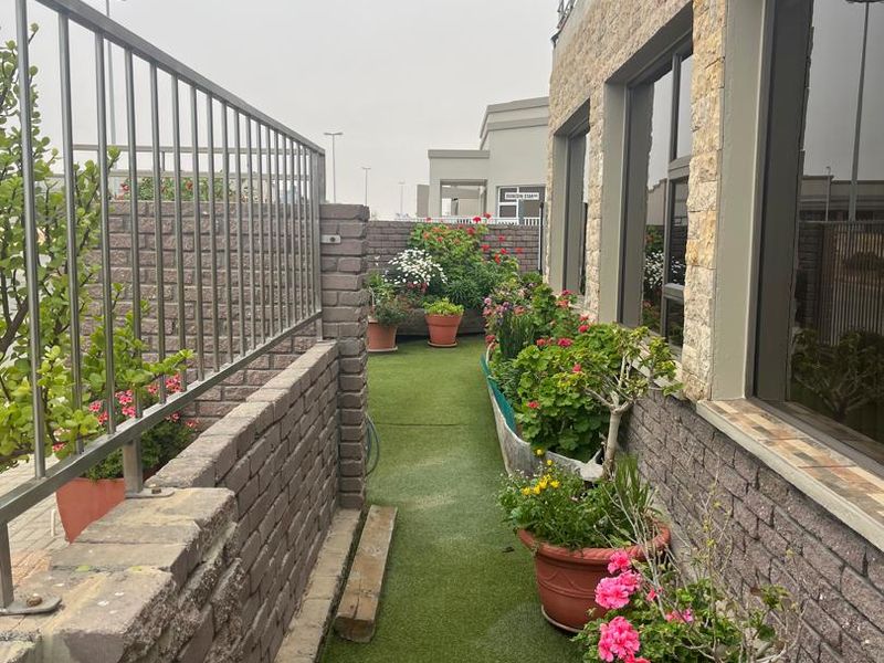 A narrow outdoor balcony area featuring artificial grass flooring, brick boundary walls, metal railings, and stone-clad exterior wall finishes.