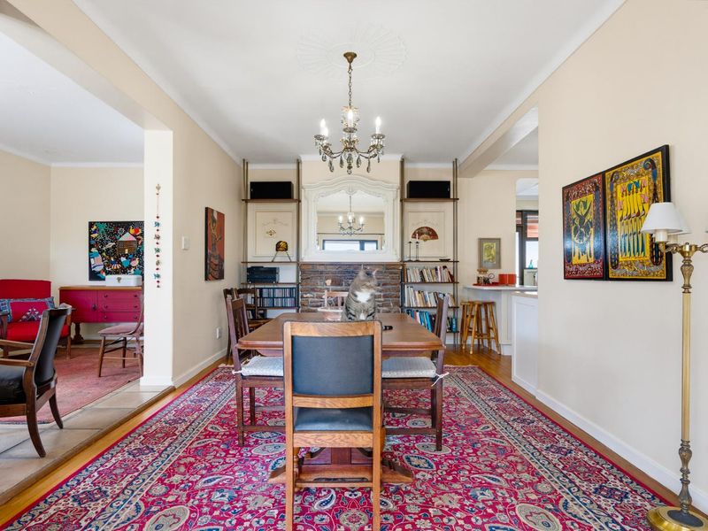 A formal dining room featuring hardwood flooring, a brick fireplace, and a decorative ceiling rose, opening into an adjacent living area.