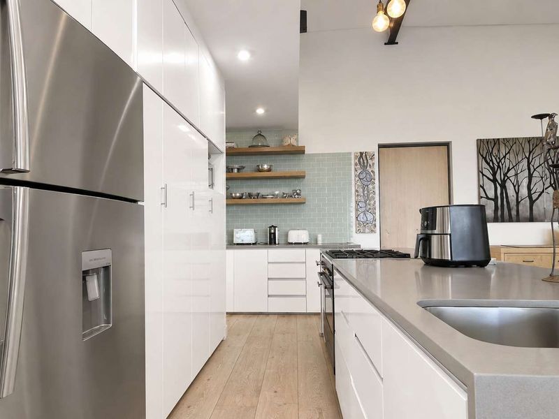 Modern kitchen featuring sleek white cabinetry, stone countertops, a central island with integrated sink and cooktop, and stylish subway tile backsplash.