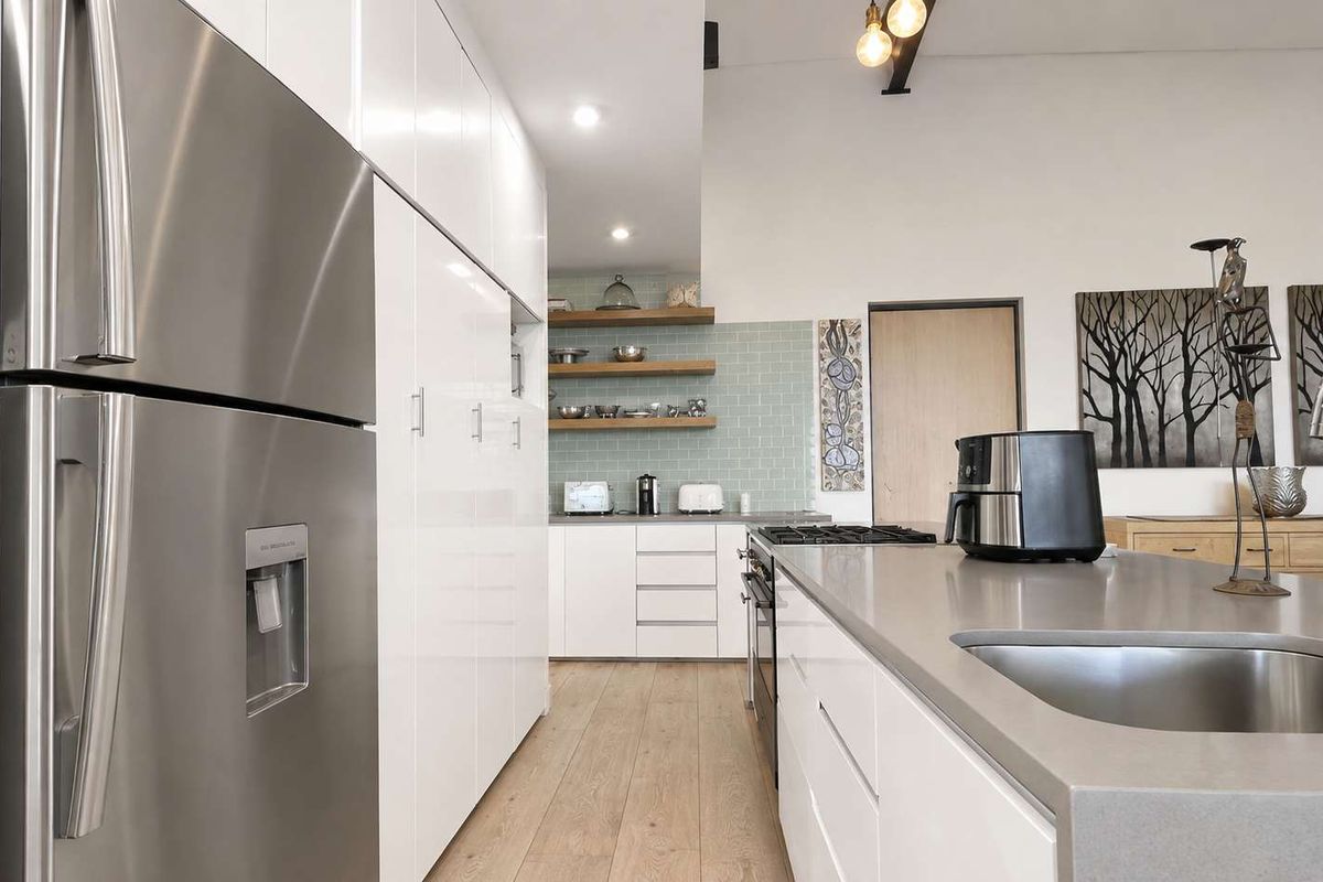 Modern kitchen featuring sleek white cabinetry, stone countertops, a central island with integrated sink and cooktop, and stylish subway tile backsplash.