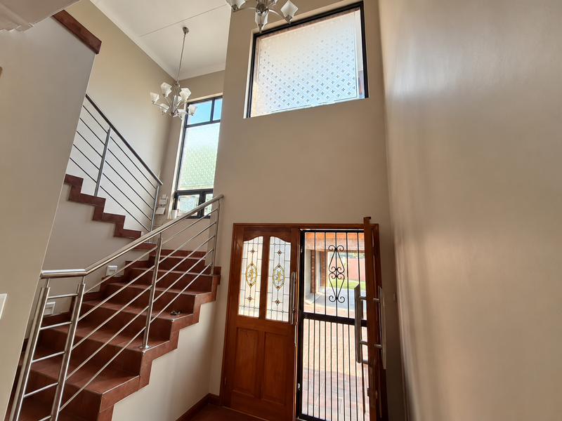 Spacious double-volume entrance hall featuring a tiled staircase with stainless steel balustrades, leaded glass front door, and abundant natural light.