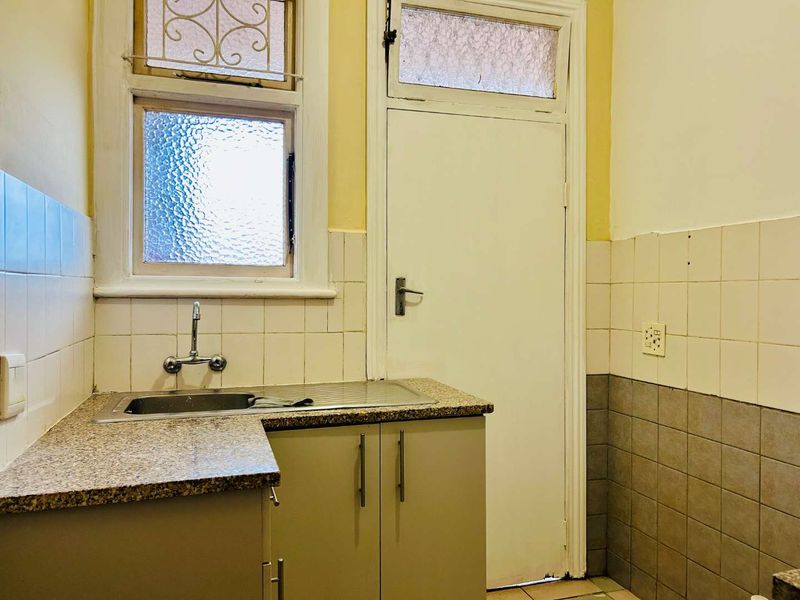 A functional scullery area featuring a stainless steel sink, granite countertop, and tiled splashback, offering a practical space for utility and preparation.