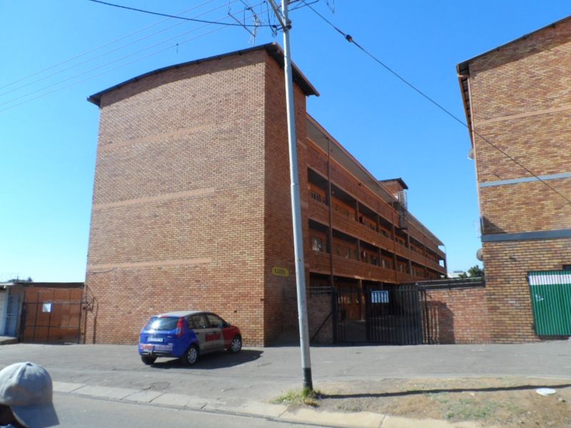 Exterior view of a multi-story face brick apartment building with a gated entrance and paved driveway area.