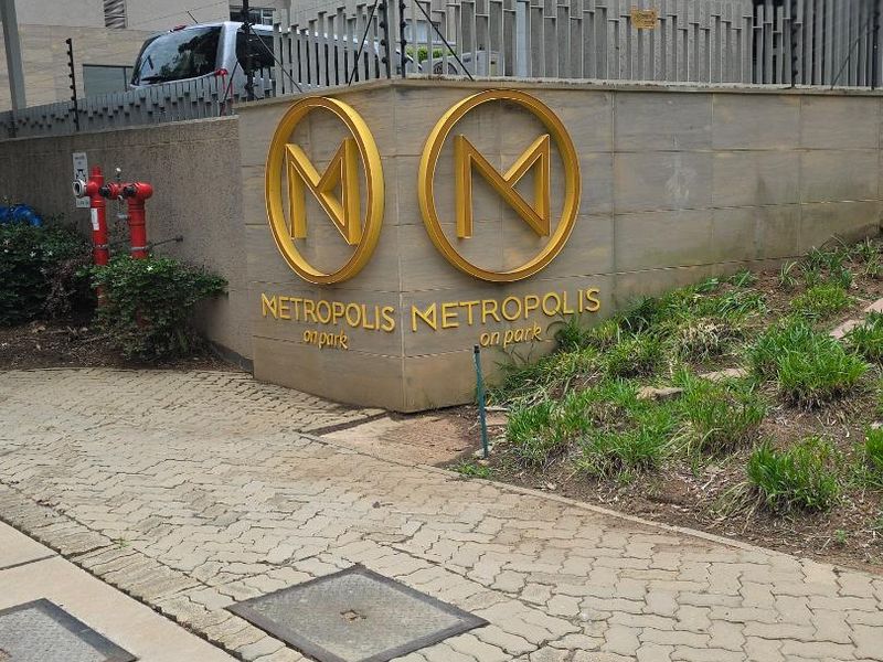 Exterior view of the Metropolis on Park apartment complex entrance, featuring building signage, a fire hydrant, and paved pedestrian access.
