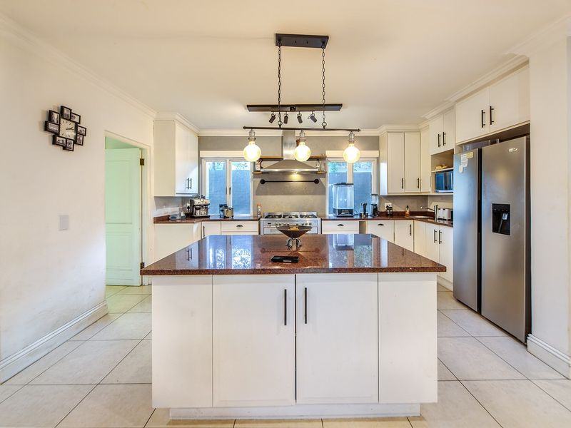 A well-appointed kitchen featuring a central island with granite countertops, ample white cabinetry, stainless steel appliances, and modern pendant lighting.