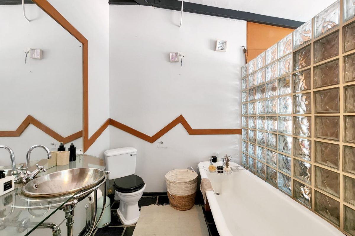 A bathroom featuring a freestanding bathtub, glass block privacy wall, pedestal sink, and toilet with dark tile flooring.