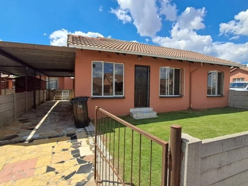 Front view of a townhouse featuring a tiled roof, carport, paved driveway, and a small front garden enclosed by a precast concrete wall.
