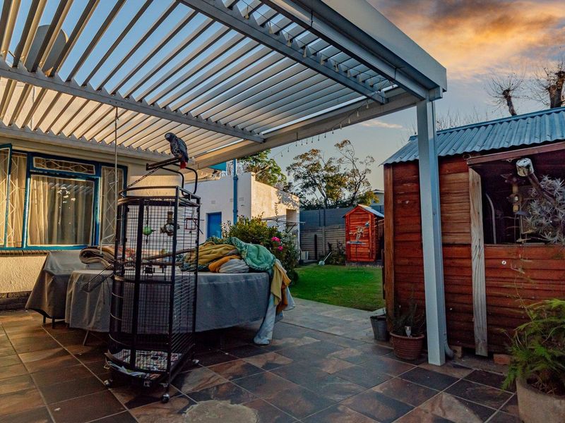 A covered patio area featuring a modern louvre roof system, tiled flooring, and an adjacent timber garden shed in the backyard.