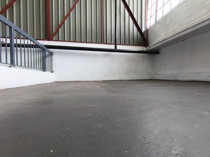 An industrial mezzanine or utility space featuring concrete flooring, metal railing, and exposed steel roof trusses with corrugated wall cladding.