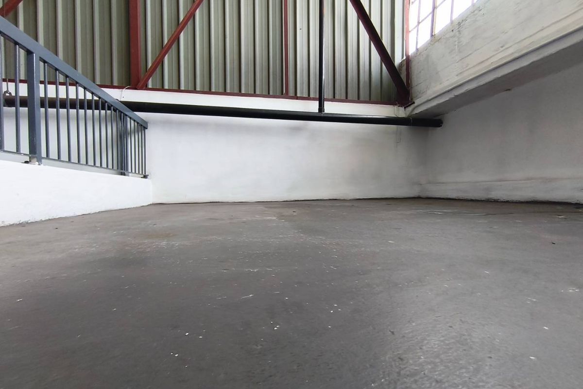 An industrial mezzanine or utility space featuring concrete flooring, metal railing, and exposed steel roof trusses with corrugated wall cladding.