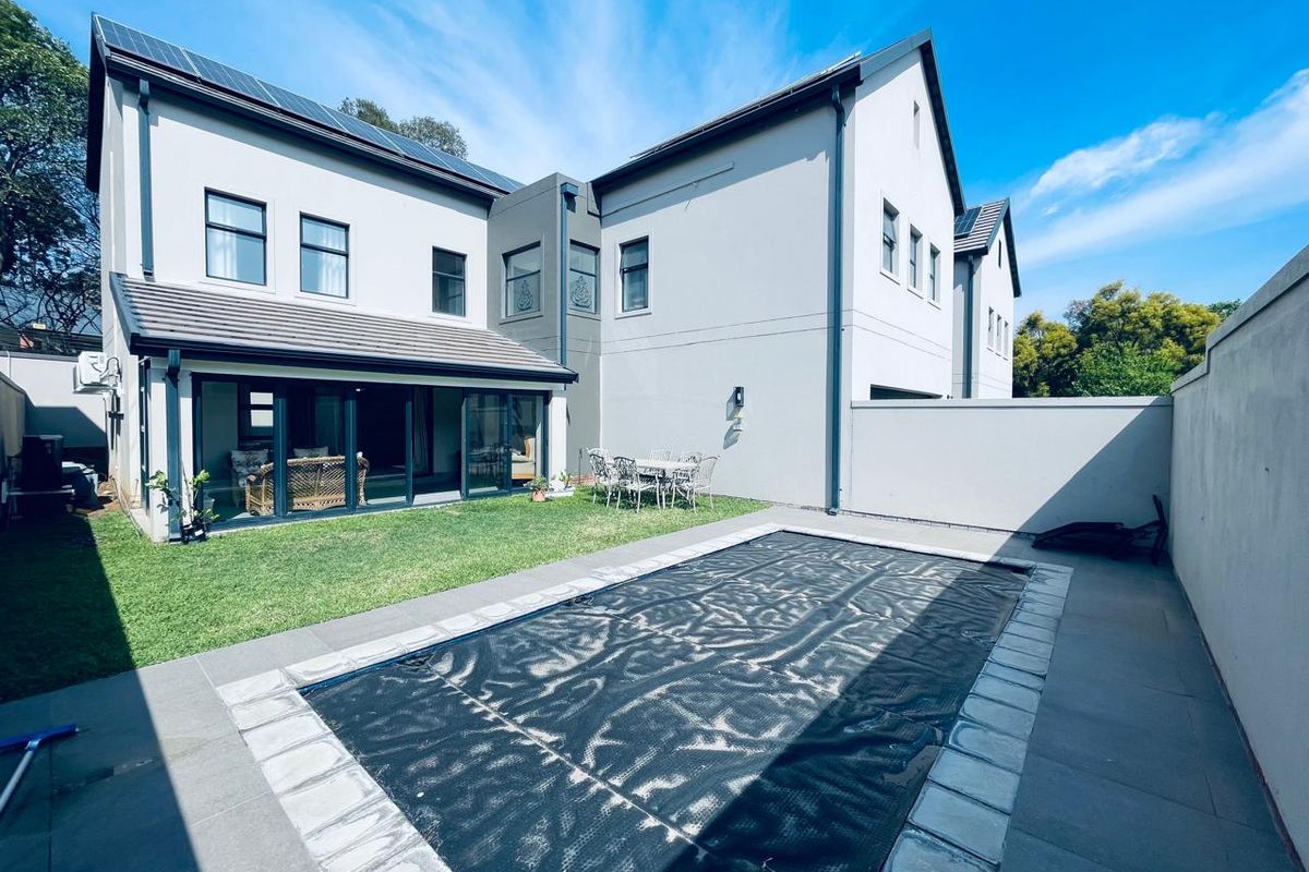 Rear exterior view of a modern cluster home featuring a swimming pool with cover, manicured lawn, and large sliding glass doors leading to the interior.