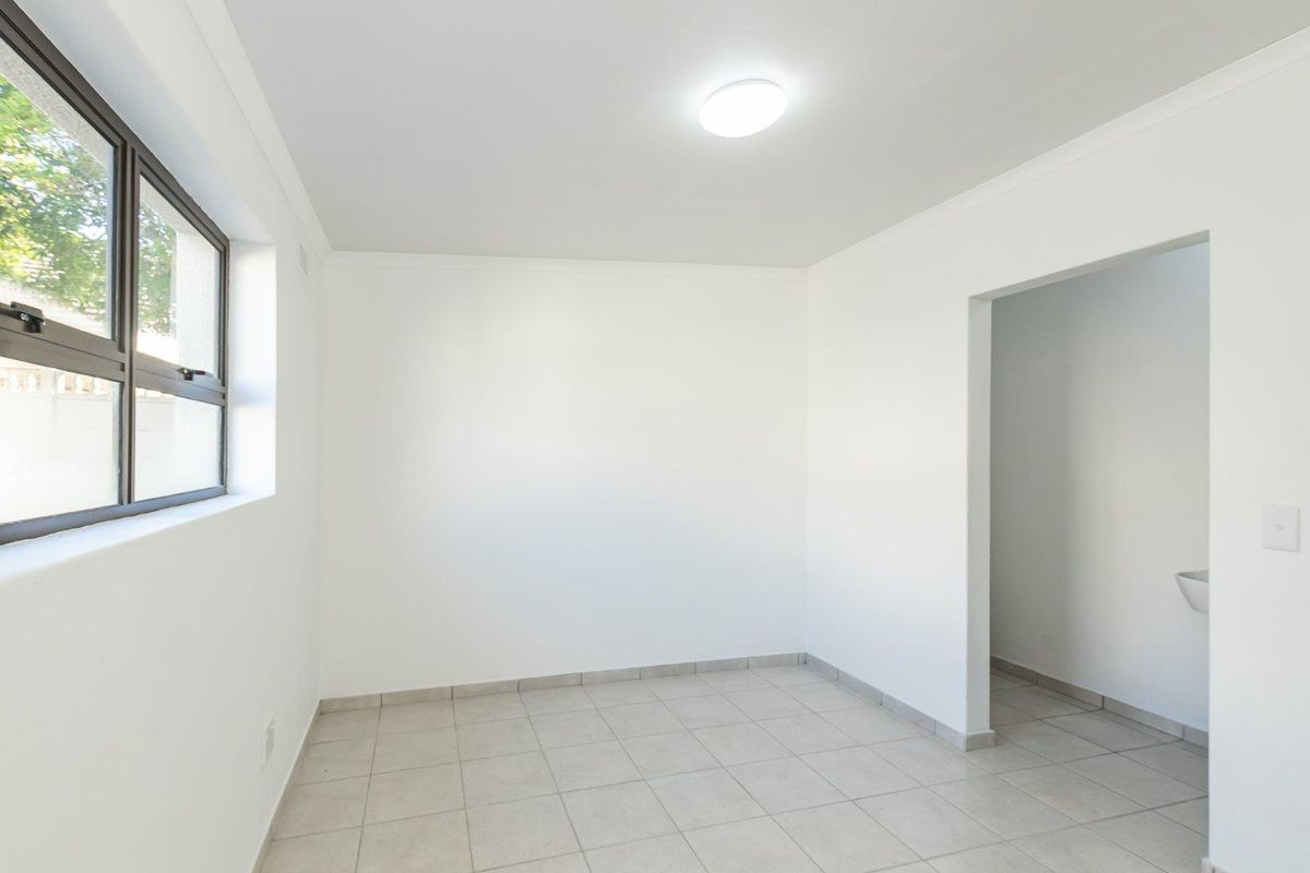 A clean, empty bedroom featuring neutral tiled flooring, white walls, and an aluminium-framed window, providing a blank canvas for interior design.