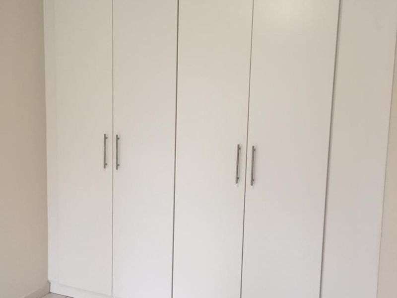 A clean, empty bedroom featuring neutral tiled flooring and a large, modern white built-in wardrobe with sleek metal handles.