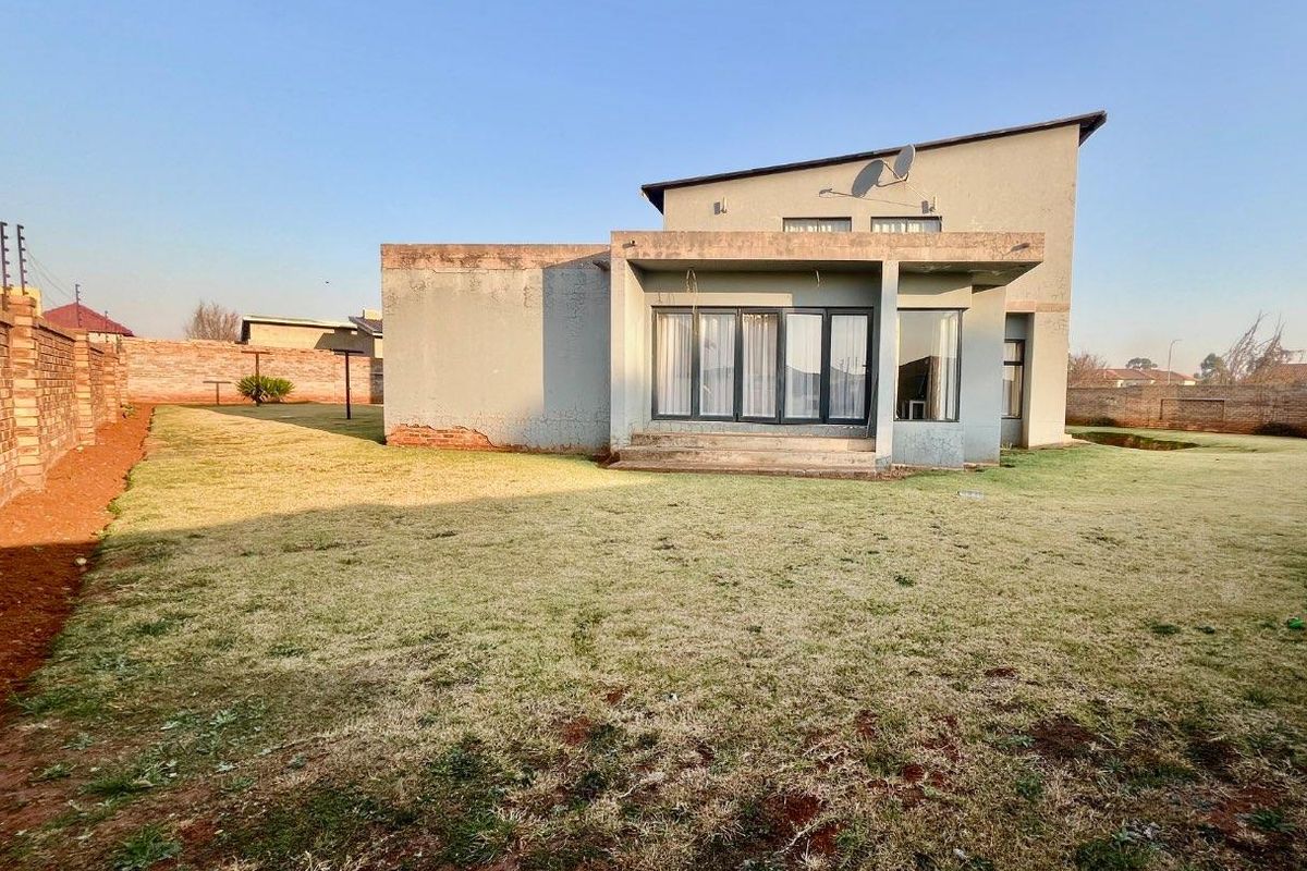 Rear view of the property featuring a concrete patio, large sliding glass doors, and a spacious backyard enclosed by a brick boundary wall.