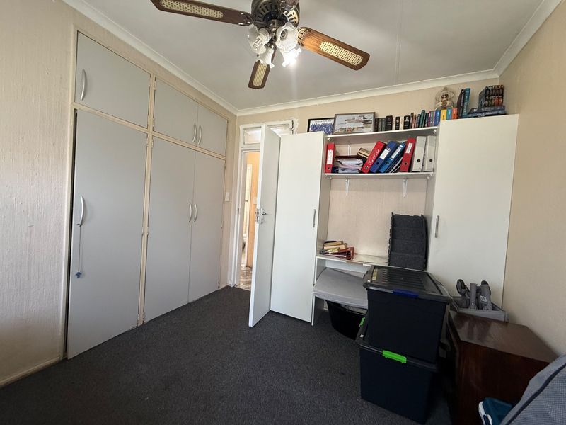 A bedroom featuring built-in cupboards, a ceiling fan, and carpeted flooring, offering functional storage space.