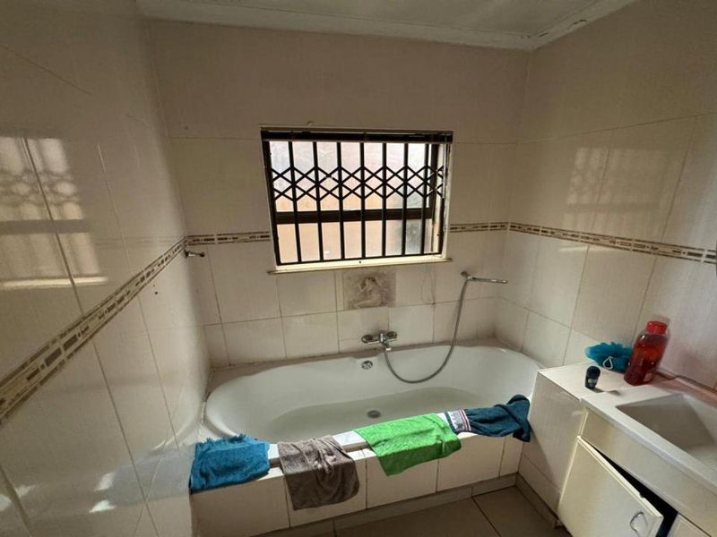 A dated bathroom featuring a built-in bathtub, vanity basin, and tiled walls, requiring cosmetic updates to improve its overall condition and appeal.