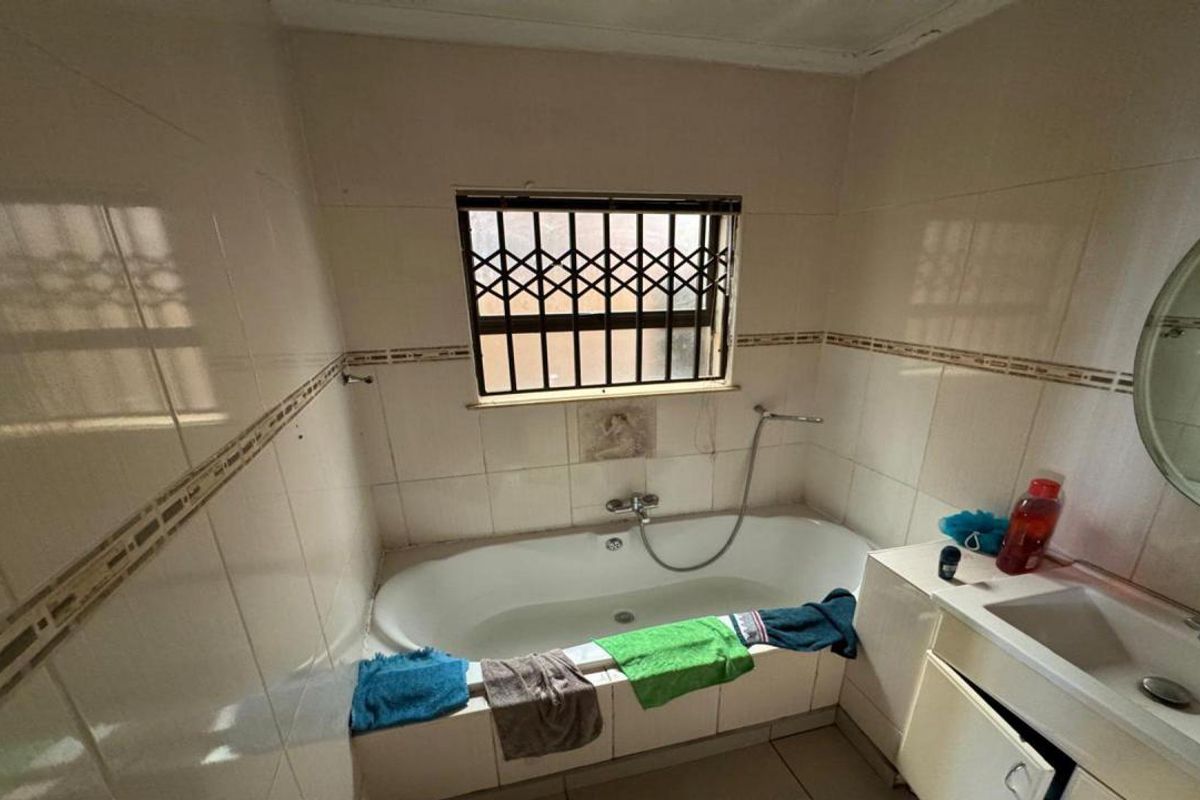 A dated bathroom featuring a built-in bathtub, vanity basin, and tiled walls, requiring cosmetic updates to improve its overall condition and appeal.