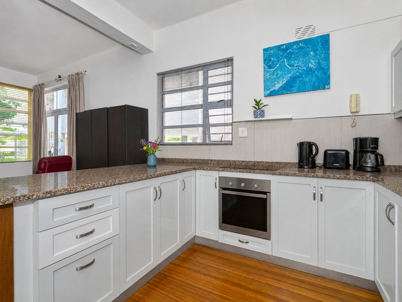 A functional kitchen featuring white cabinetry, granite countertops, built-in oven, electric hob, and warm hardwood flooring, offering a clean and practical workspace.