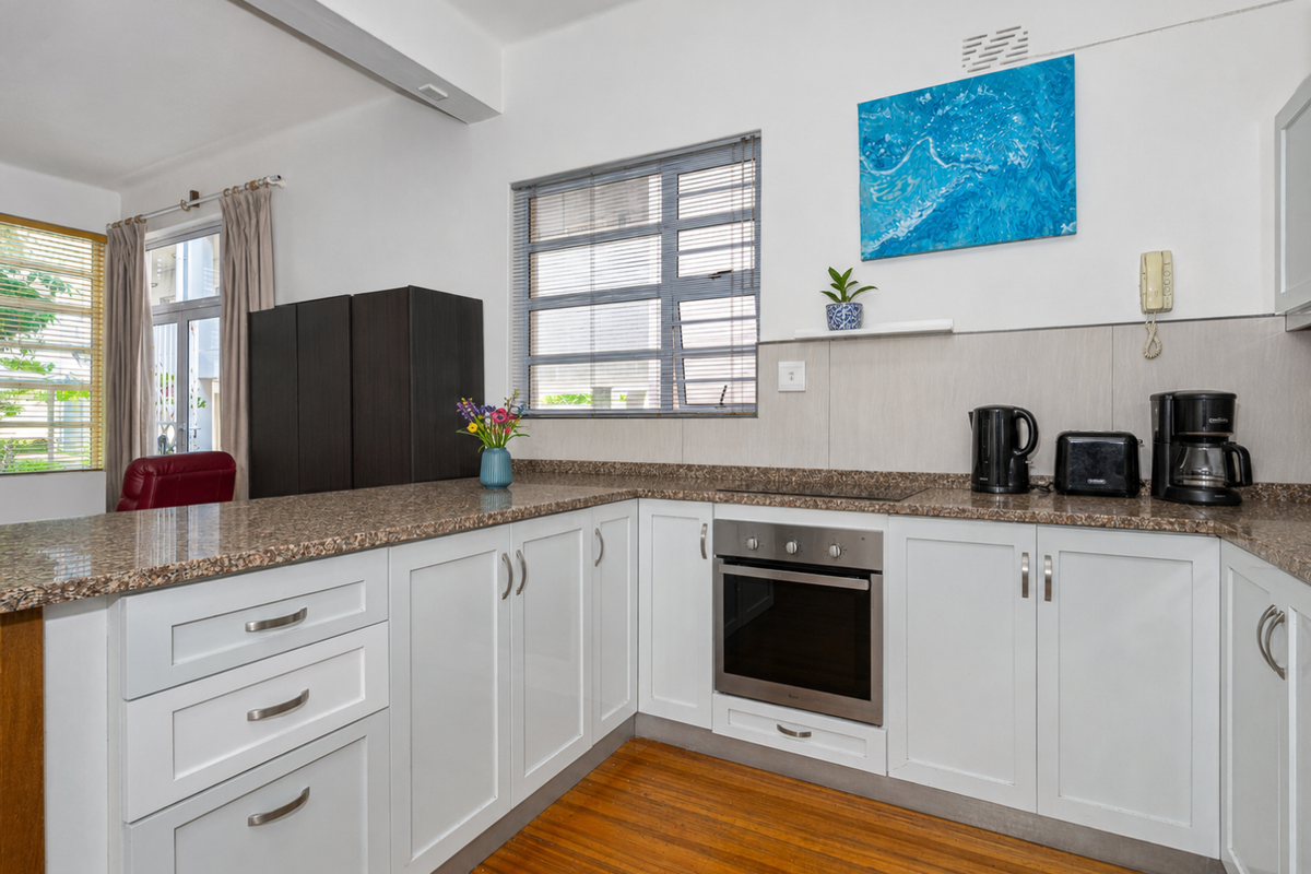 A functional kitchen featuring white cabinetry, granite countertops, built-in oven, electric hob, and warm hardwood flooring, offering a clean and practical workspace.