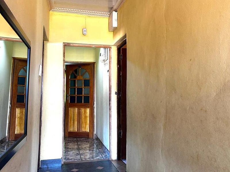 A narrow residential hallway featuring dark tiled flooring, decorative ceiling molding, and a traditional timber door leading to an adjacent room.