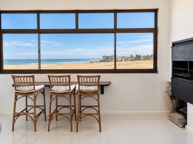 Bright living area featuring a built-in fireplace, tiled flooring, and a large window offering expansive ocean and beach views.