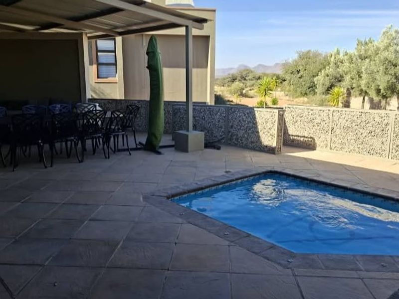 Outdoor entertainment area featuring a covered patio, paved terrace, and a swimming pool with decorative stone walling.