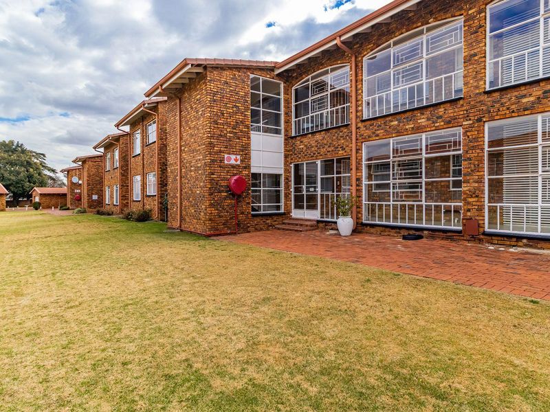 Rear view of a multi-story brick townhouse complex featuring large steel-framed windows, a paved patio area, and an expansive communal lawn.