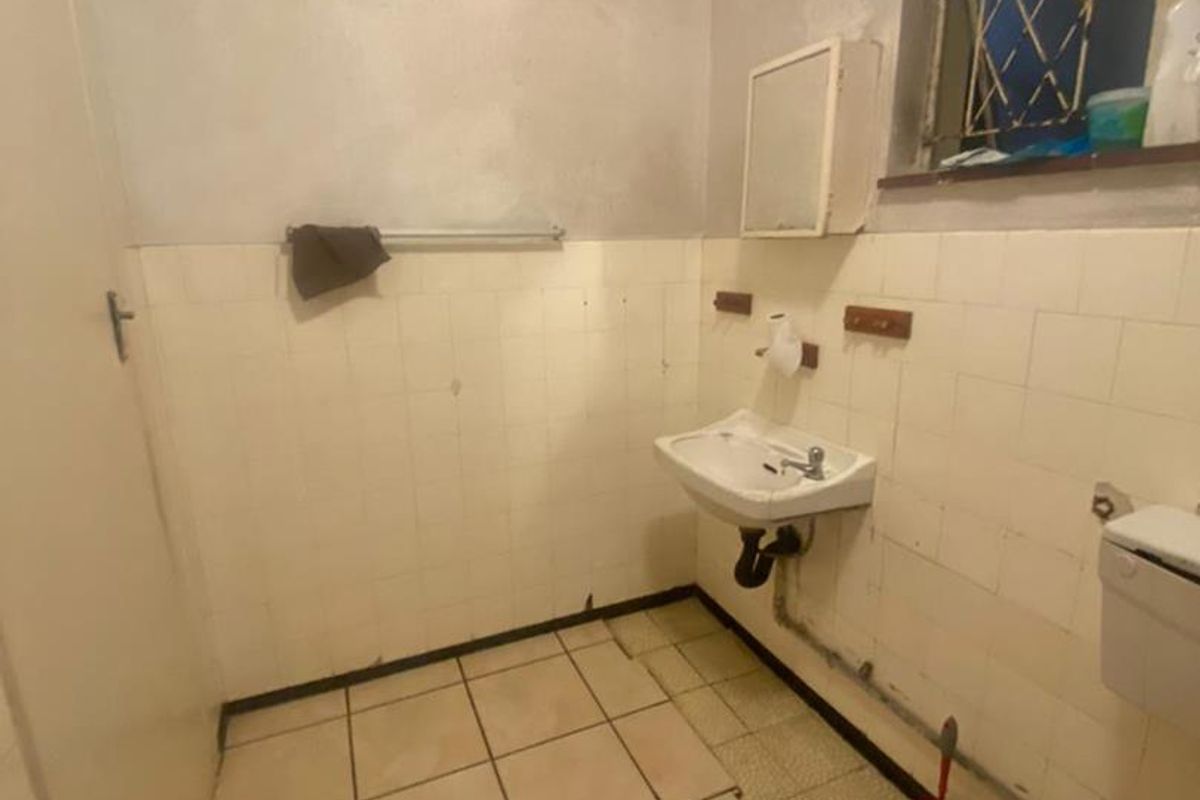 A dated bathroom featuring original wall tiling, a wall-mounted basin, and a standard toilet, requiring significant renovation and cosmetic updates.
