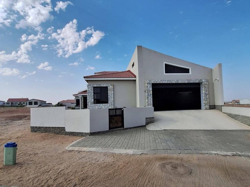 Modern single-story house featuring stone cladding accents, a paved driveway, and a secure garage, situated in a developing residential area.