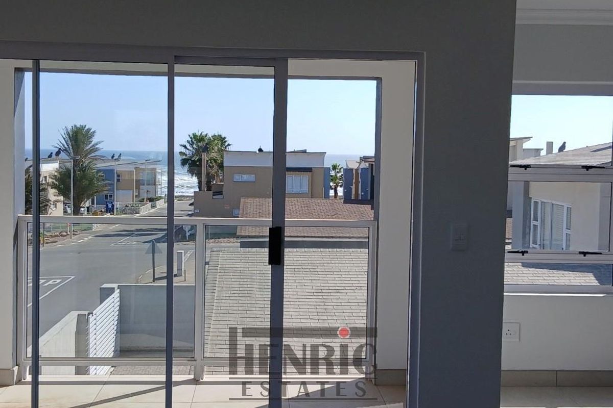 A bright living area featuring large sliding glass doors that open onto a balcony, offering clear views of the surrounding neighbourhood and coastline.