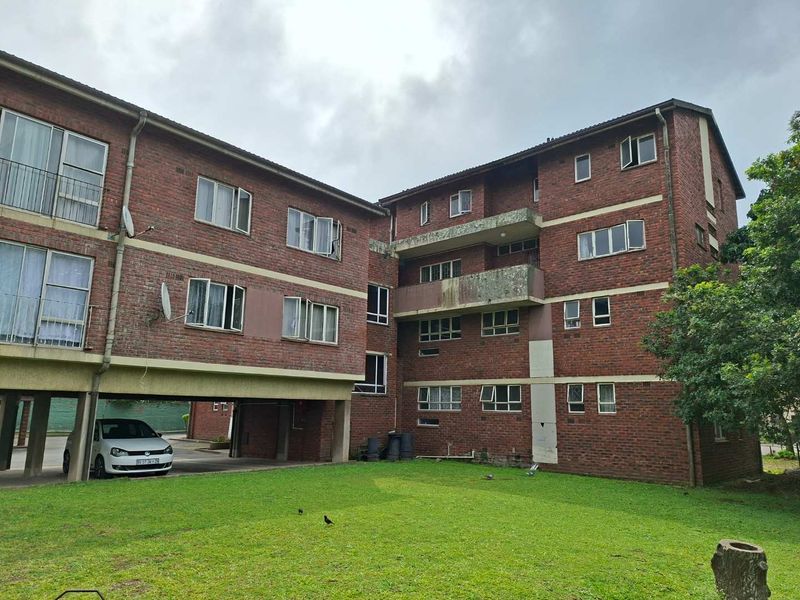 Rear view of a multi-story brick apartment building featuring concrete balconies, aluminium windows, and a shared ground-level lawn area.