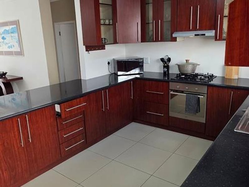 A functional kitchen featuring dark wood cabinetry, granite countertops, built-in oven, gas hob, and tiled flooring, offering ample workspace and storage.