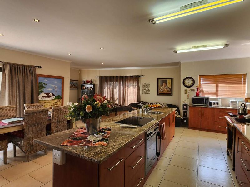 Spacious open-plan kitchen and dining area featuring a large granite-topped island, wooden cabinetry, and tiled flooring with direct access to the patio.
