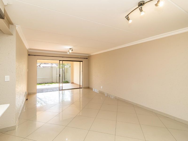 Spacious, light-filled living area featuring neutral tiled flooring, coved cornicing, and large sliding glass doors providing direct access to the outdoor patio.