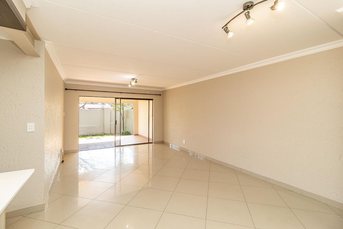 Spacious, light-filled living area featuring neutral tiled flooring, coved cornicing, and large sliding glass doors providing direct access to the outdoor patio.