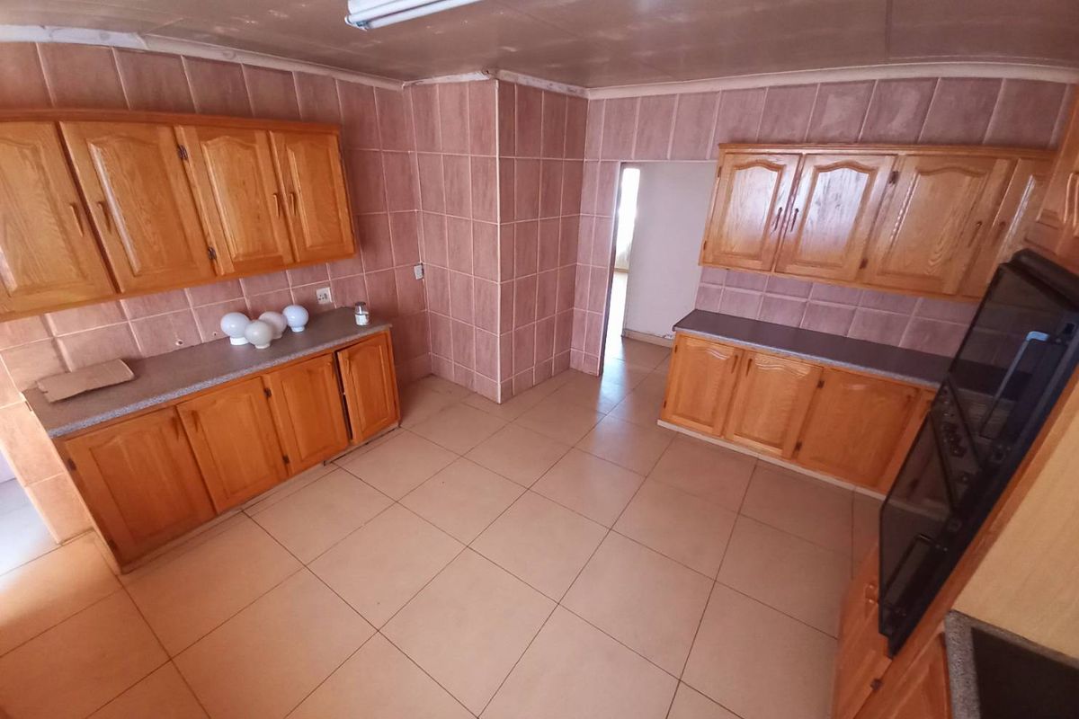 A dated kitchen featuring wooden cabinetry, tiled walls, and tiled flooring, offering a functional layout ready for modernization.