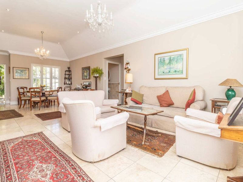 Spacious open-plan living and dining area featuring vaulted ceilings, tiled flooring, elegant chandeliers, and plantation shutters, offering a bright and comfortable living space.