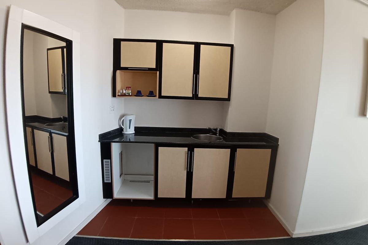 A compact kitchenette featuring dark stone countertops, built-in cabinetry, and a stainless steel sink, set against a tiled floor area.