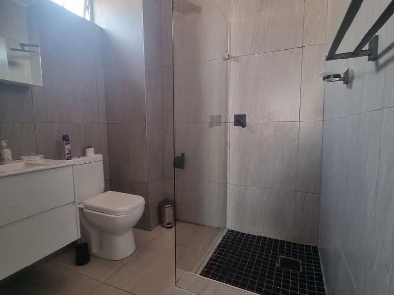Modern bathroom featuring a walk-in shower with a glass screen, rain shower head, wall-mounted vanity, and neutral floor-to-ceiling tiling.