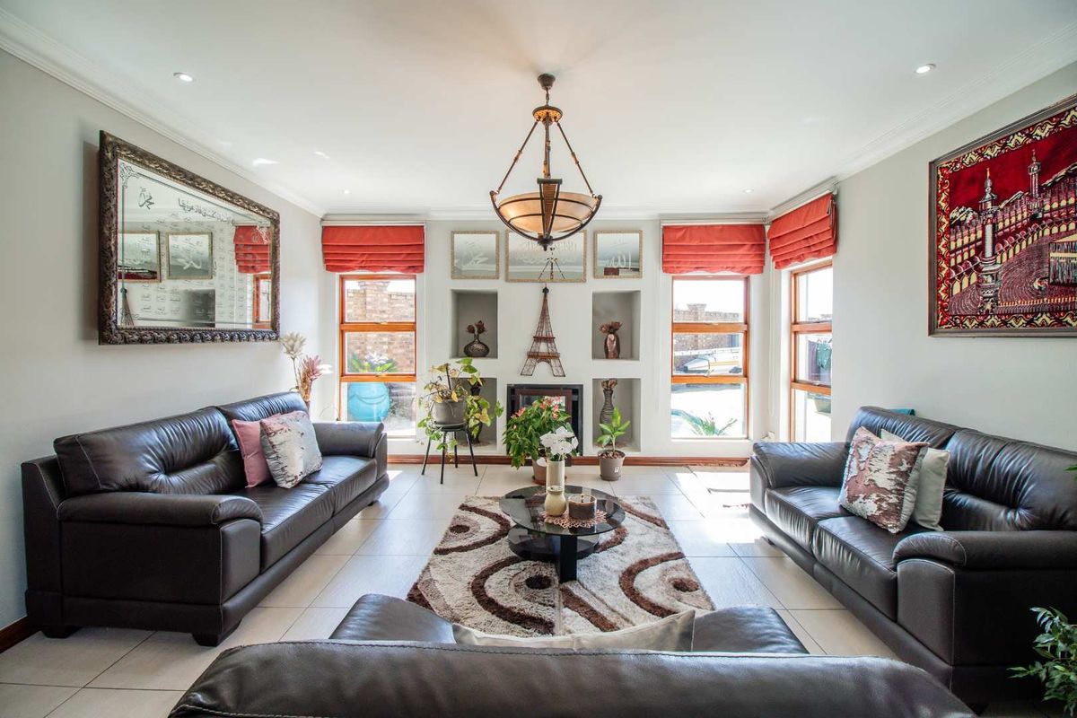 A well-lit living room featuring tiled flooring, recessed wall niches, large windows with wooden frames, and a central pendant light fixture.