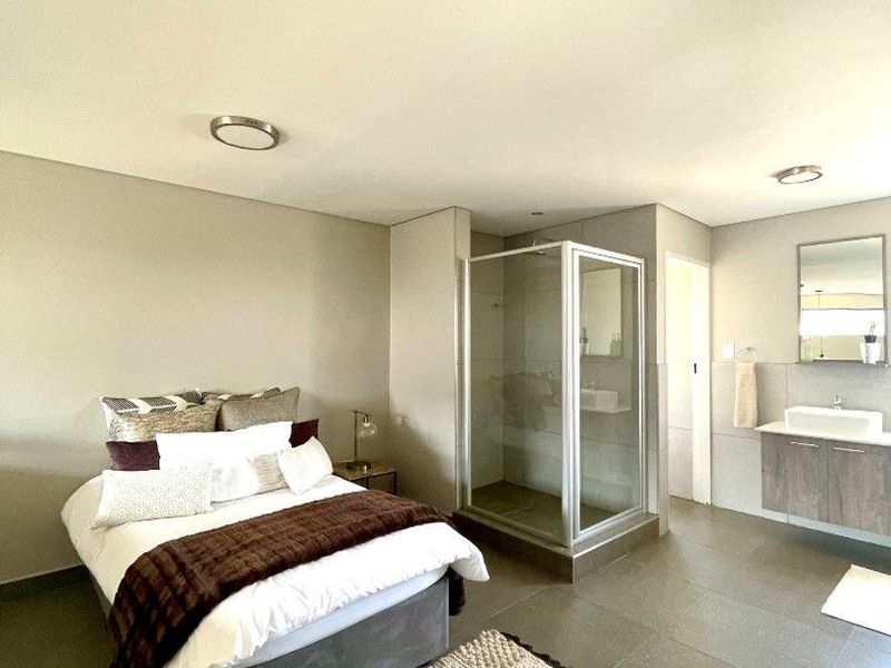 Spacious bedroom featuring an open-plan en-suite bathroom with a glass-enclosed shower, modern vanity, and neutral tiled flooring throughout.