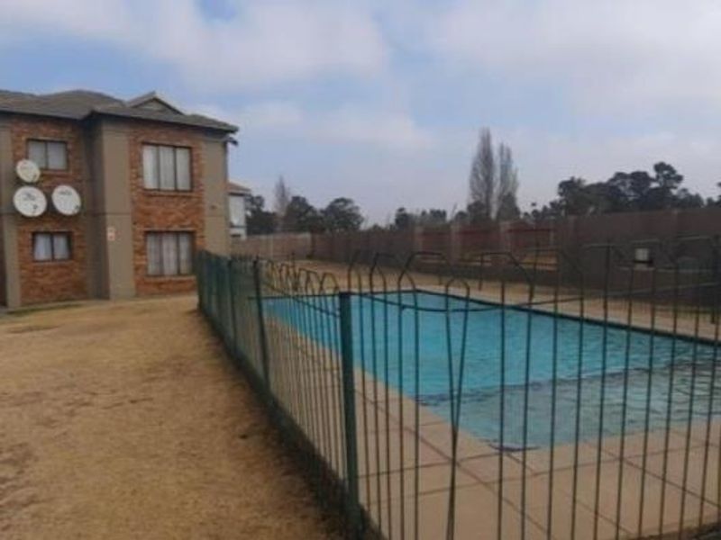 Communal swimming pool area with perimeter fencing and brick apartment building facade.