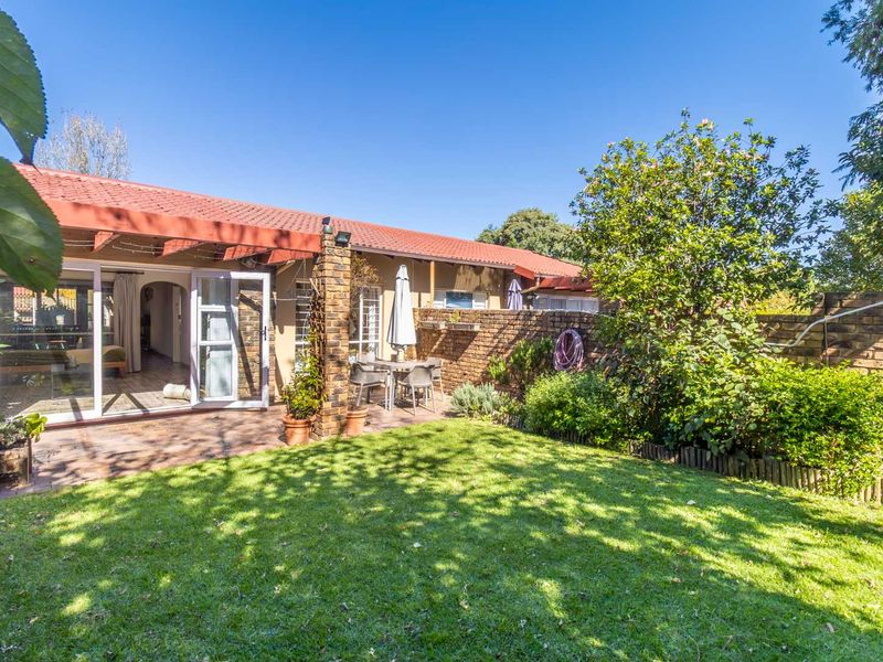 A private rear garden featuring a paved patio area, established lawn, and brick boundary walls, accessible via sliding glass doors from the main living space.