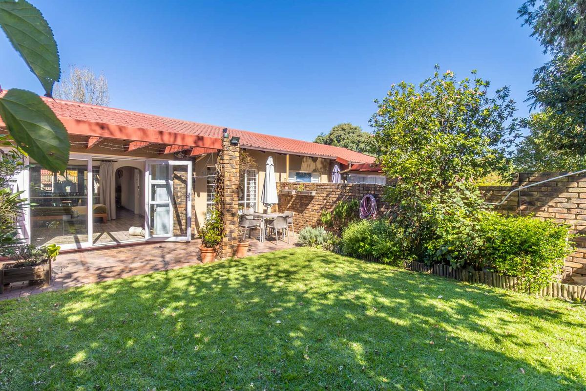 A private rear garden featuring a paved patio area, established lawn, and brick boundary walls, accessible via sliding glass doors from the main living space.