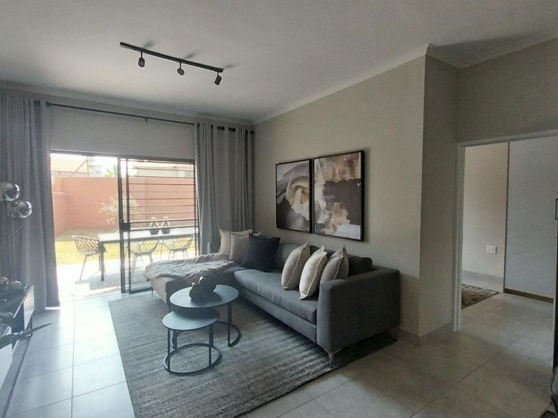 A well-maintained living room featuring tiled flooring, modern track lighting, and a large sliding glass door providing direct access to the rear patio.