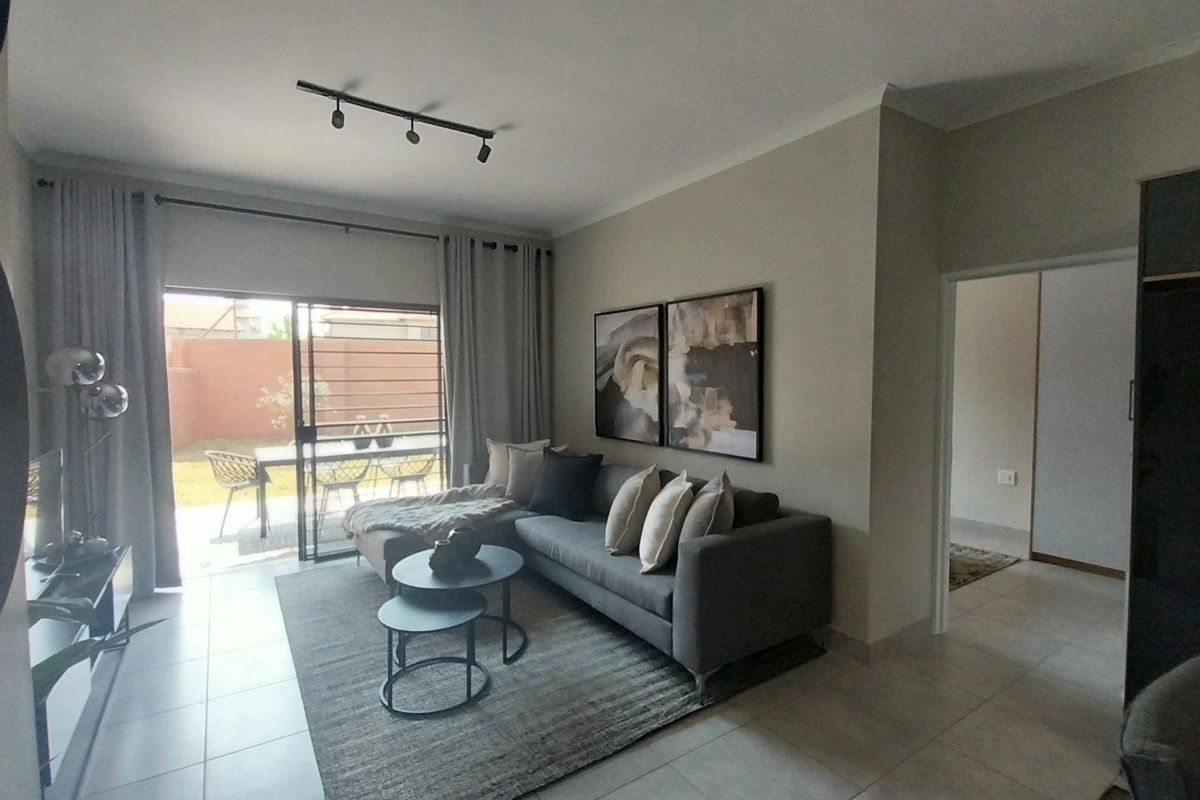 A well-maintained living room featuring tiled flooring, modern track lighting, and a large sliding glass door providing direct access to the rear patio.