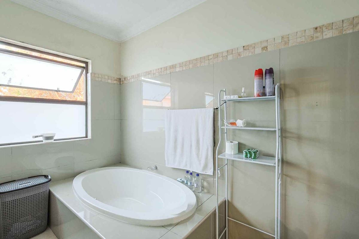 A functional bathroom featuring a built-in bathtub with tiled surround and splashback, complemented by an awning window for natural light and ventilation.