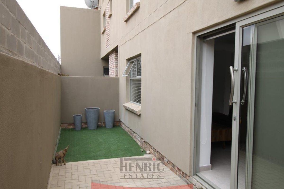 A compact rear courtyard featuring paved flooring, artificial grass, and a sliding glass door providing access to the interior living space.