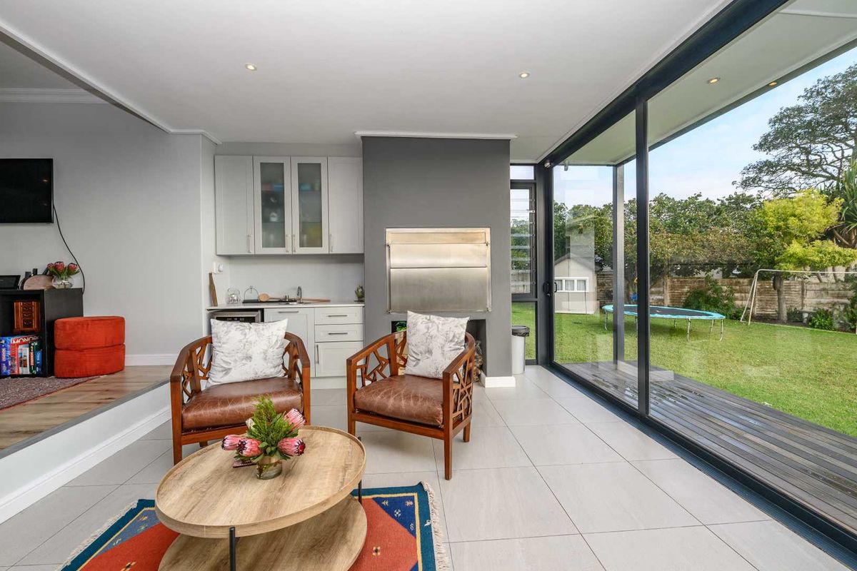 Modern living area featuring a built-in stainless steel braai, cabinetry, and large sliding glass doors opening onto a landscaped garden.