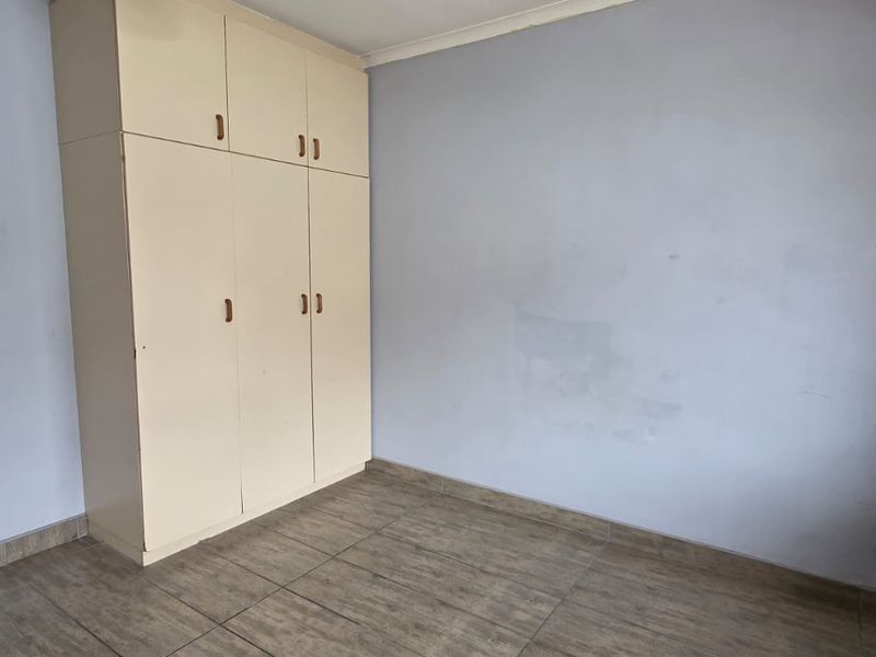 An empty bedroom featuring tiled flooring and built-in cupboards, providing a blank canvas for personalization.
